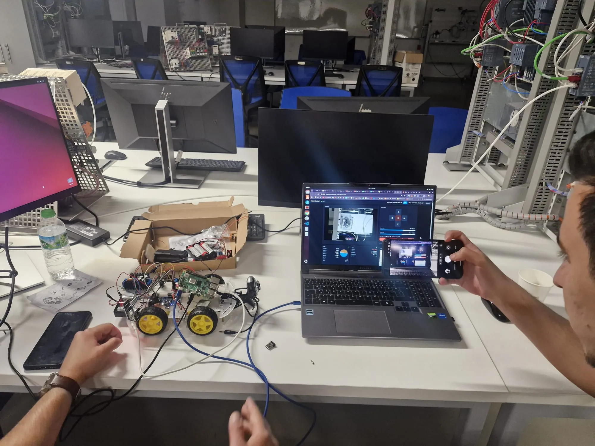 Lab scene with the physical rover wired to a laptop running the dashboard