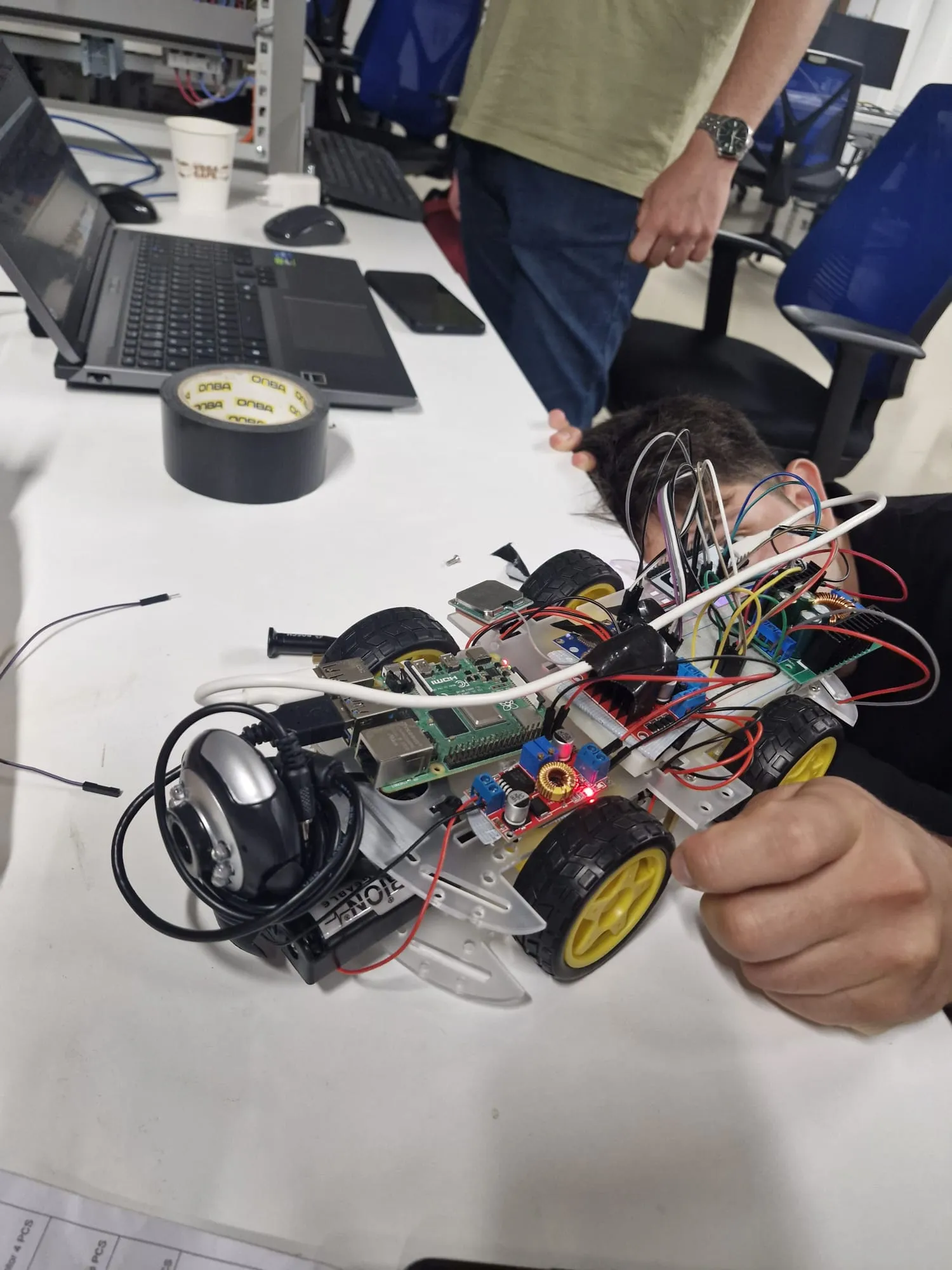 The rover held up close, showing the wiring, Raspberry Pi, buck converters and front camera